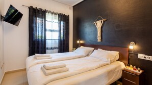 Un lit double avec du linge de lit blanc, une table de chevet avec une lampe et un téléviseur fixé au mur.