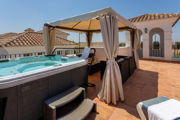 Una terraza en la azotea con jacuzzi, mobiliario exterior y un área techada.