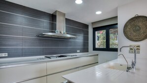 Uma cozinha moderna com coifa de aço inoxidável, armários brancos e uma janela com vista para o verde.