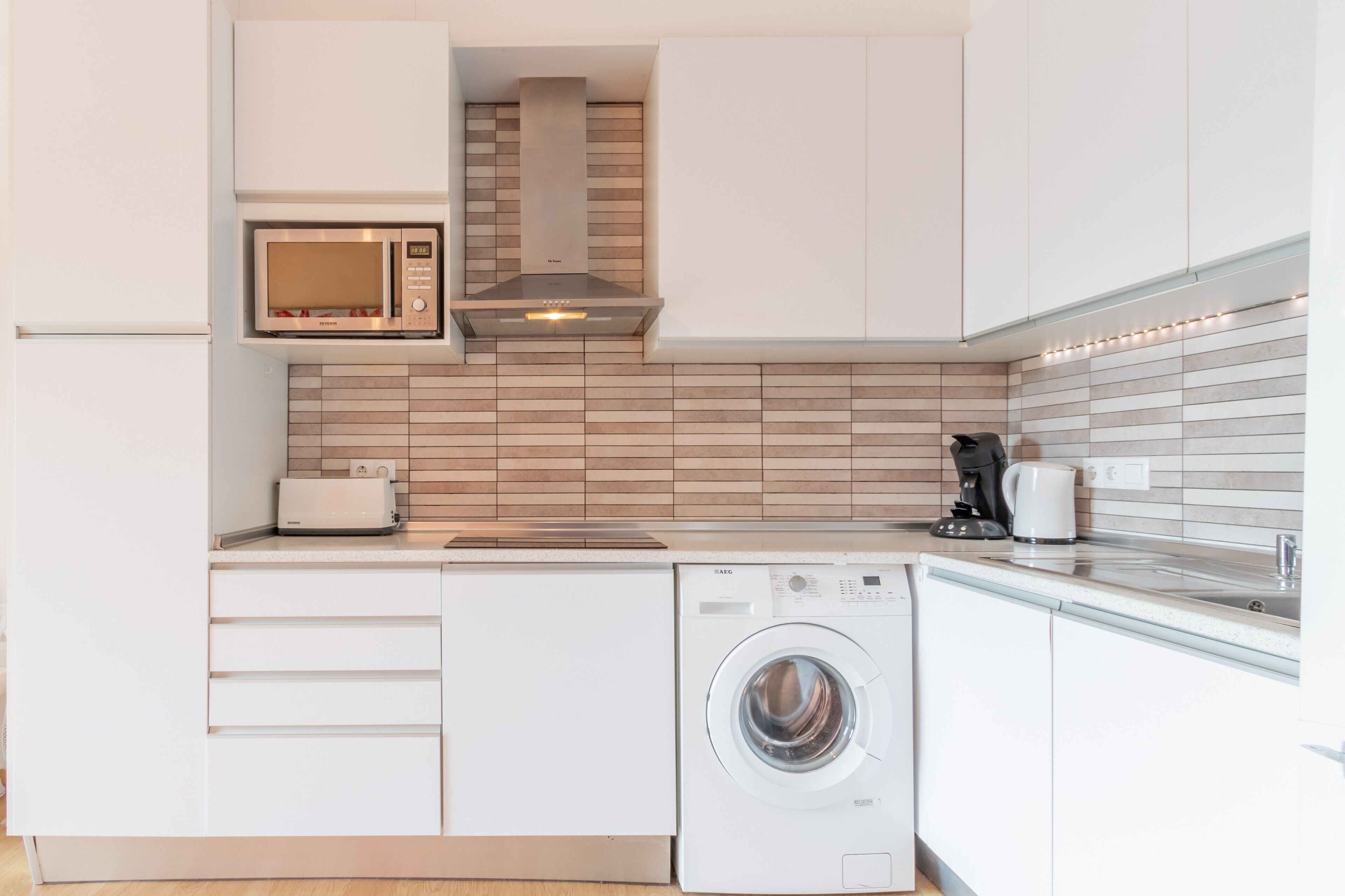 Een kleine keuken met een magnetron, broodrooster en wasmachine.