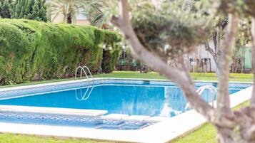 Una piscina con escalera, rodeada de césped y árboles bien cuidados.