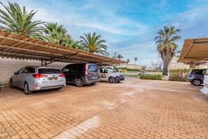 Un estacionamiento con varios coches, palmeras y un paseo techado.