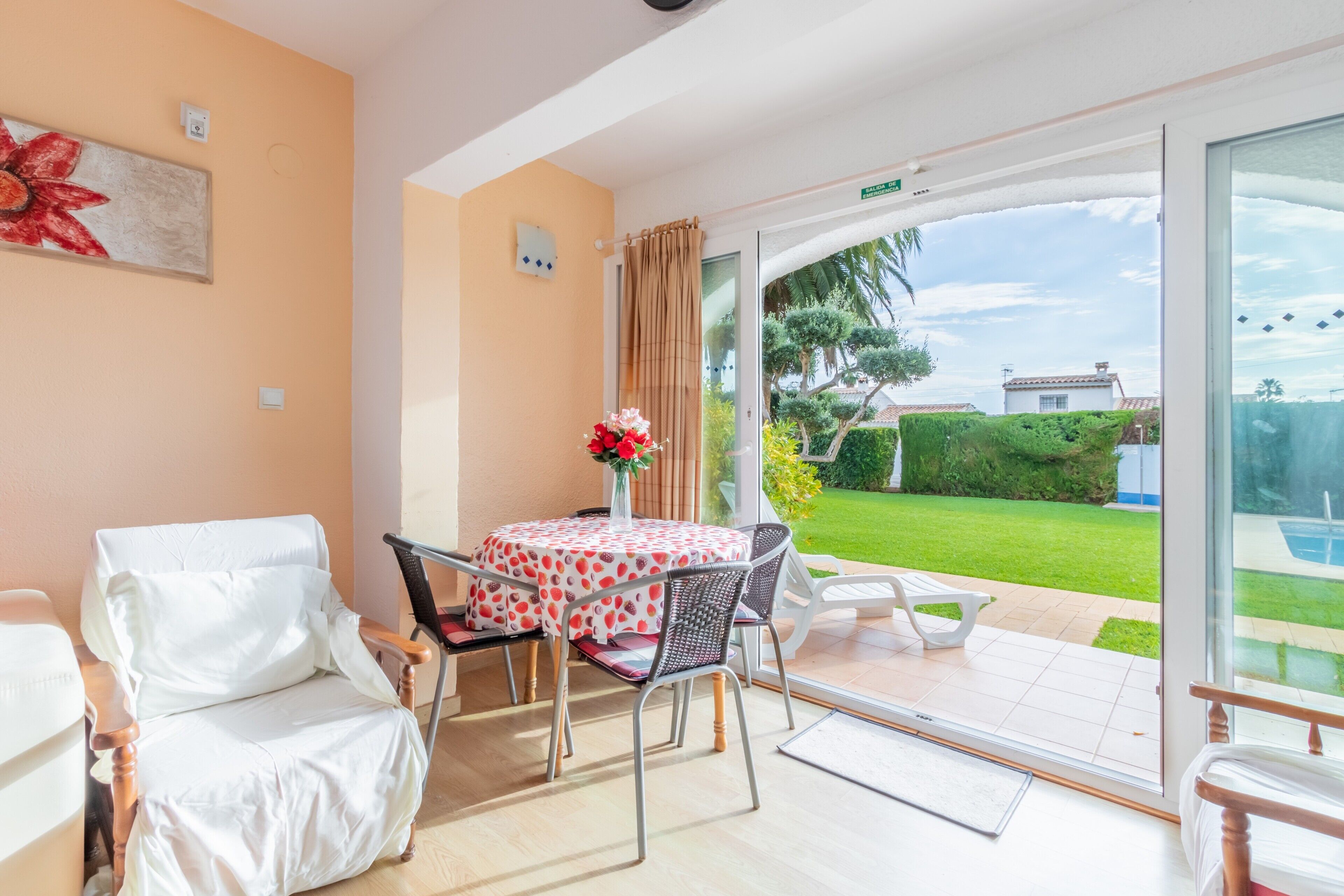 Una habitación con una mesa y sillas, un ventanal con vistas a un jardín y una puerta que da al exterior.
