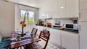 Una cocina moderna con armarios blancos, una mesa de comedor con sillas, un microondas y una ventana con vistas a zonas verdes.