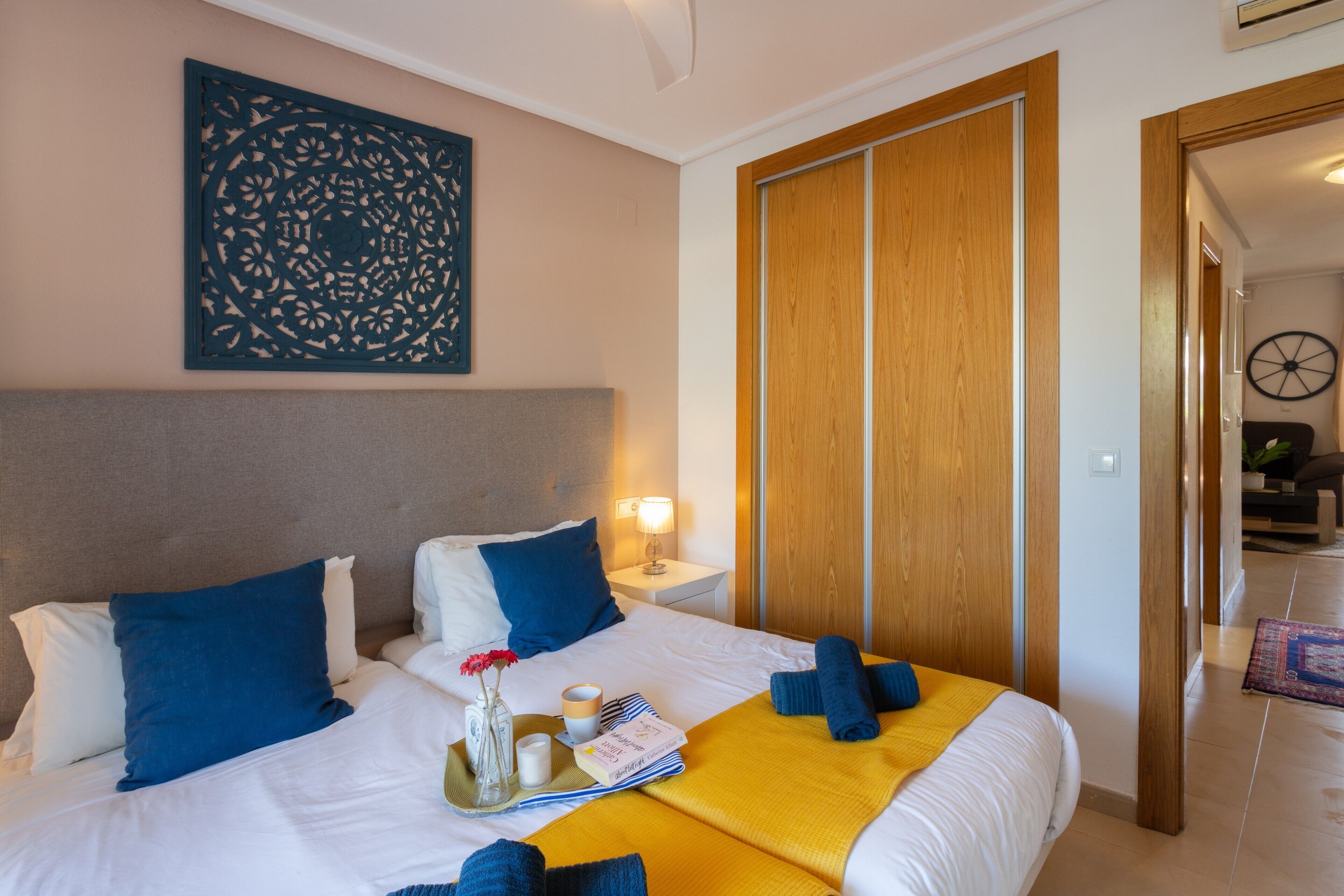 Ein Hotelzimmer mit Bett, Nachttisch, einem Kunstwerk an der Wand, einem Holzschrank und einer Tür zu einem anderen Raum.