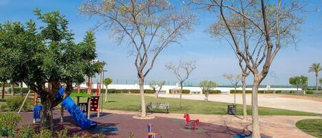 A playground with slides and swings, surrounded by trees and a clear sky.