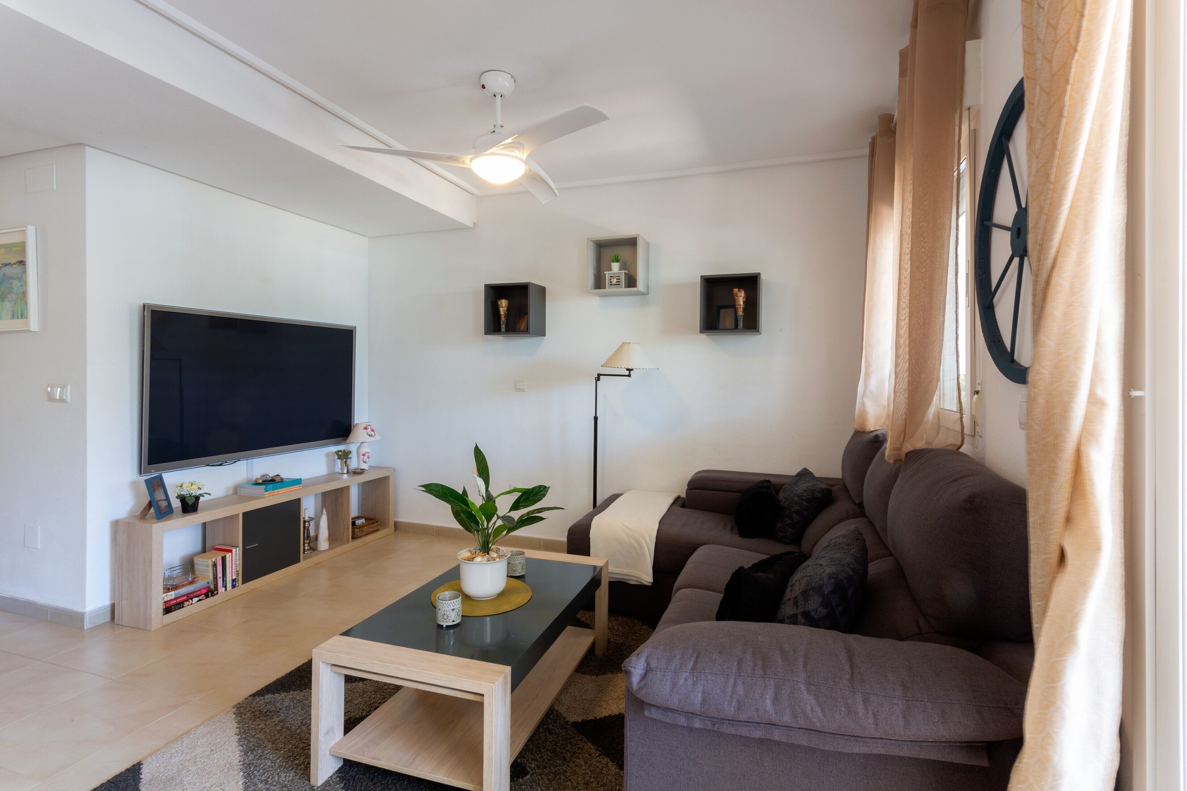 Ein Wohnzimmer mit Flachbildfernseher, Deckenventilator, Sofa, Couchtisch und Stehlampe.