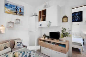 A modern, well-lit room with a wooden desk, a television, a bed, and a wall-mounted shelf with decorative items.