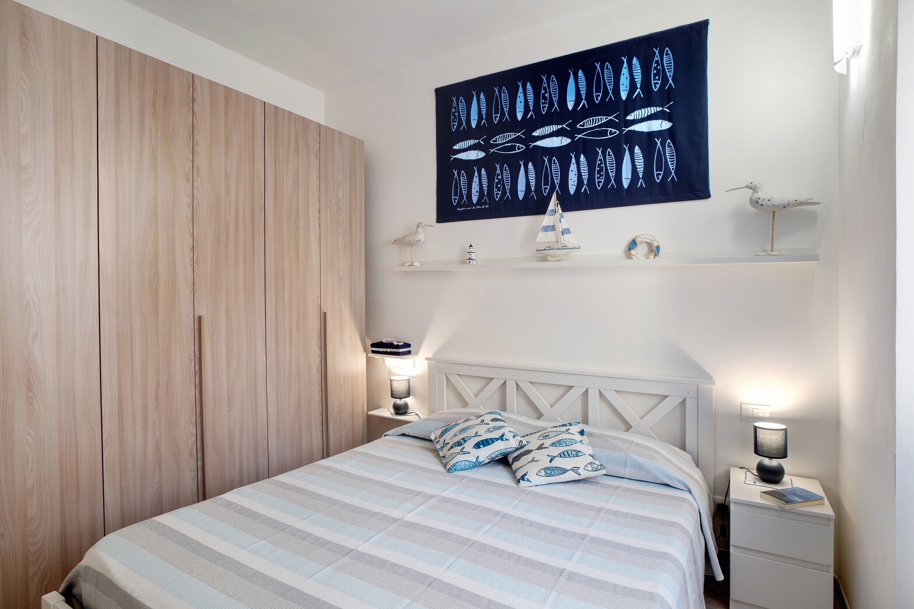 A bedroom with a bed, nightstands, a shelf with decorative items, and a wall art piece.
