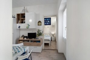 A compact, well-lit room with a desk, chair, bed, and a small bedside table.
