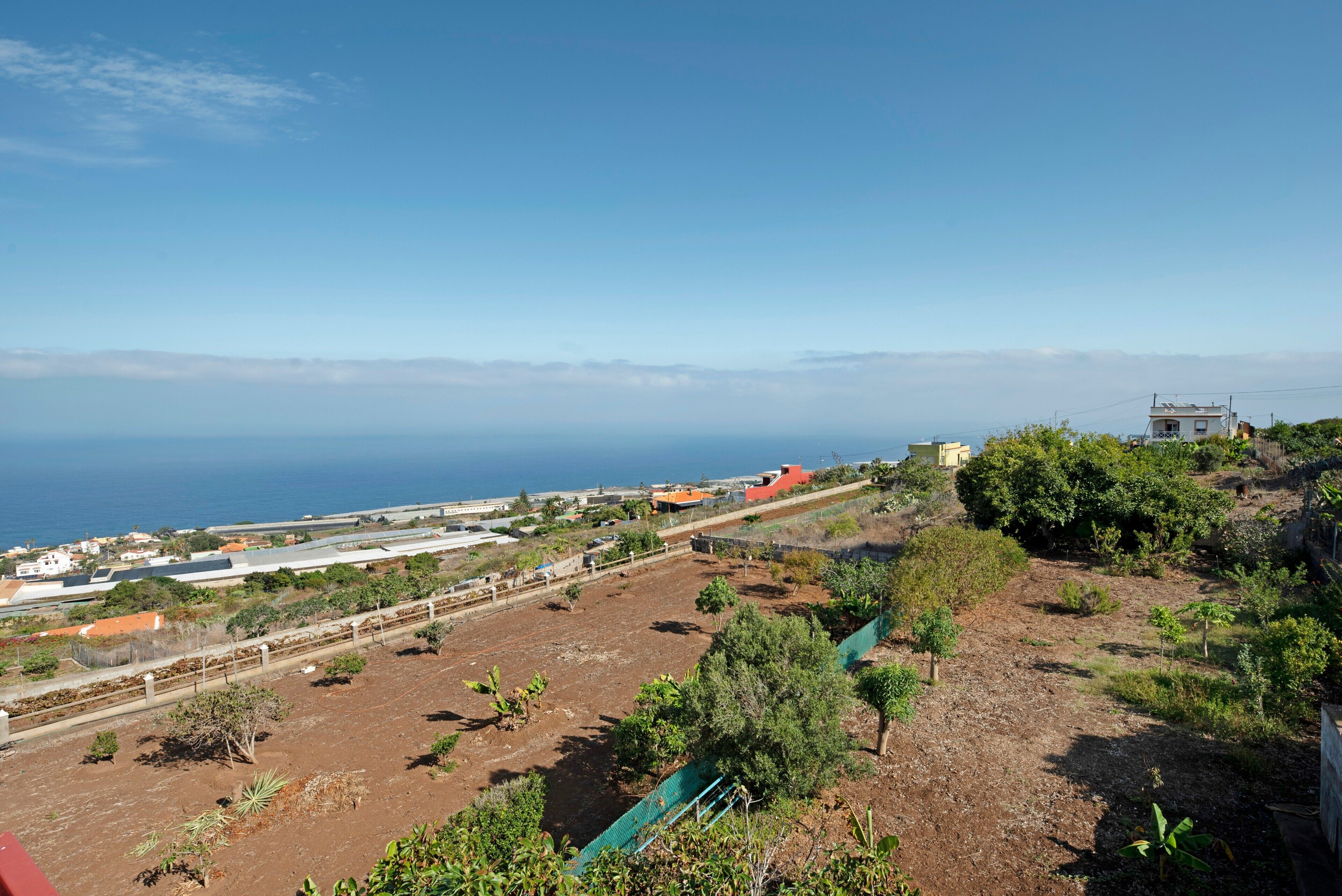 A coastal landscape with a view of the sea, a fenced property, and a building with a red roof.