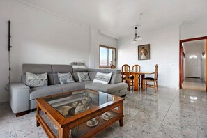 Ein Wohnzimmer mit grauem Sofa, Holztisch und einem Essbereich mit Stühlen und Tisch.