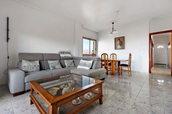 A living room with a grey sofa, wooden coffee table, and a dining area with chairs and a table.