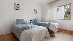 Een slaapkamer met twee bedden, een nachtkastje, een raam en ingelijste foto’s aan de muur.