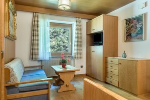 Una habitación con un banco de madera, una mesita con un florero, un armario y un cuadro en la pared.