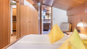 A hotel room with a bed, wooden wardrobe, a chair, a nightstand, and a mirror.