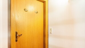 Une porte en bois avec une poignée et une serrure en laiton, un interphone et un interrupteur à proximité sur le mur.