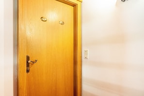 Une porte en bois avec une poignée et une serrure en laiton, un interphone et un interrupteur à proximité sur le mur.