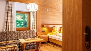 Une pièce chaleureuse avec un plafond en bois, un canapé, une petite table, un lit avec des coussins jaunes et une fenêtre donnant sur des arbres.