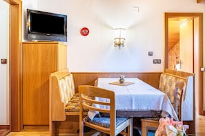 Un espace repas comprenant une table, des chaises, un téléviseur et un luminaire fixé au mur.