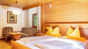 Une pièce aux murs lambrissés, comprenant un lit, une chaise, une petite table et une fenêtre avec des rideaux.