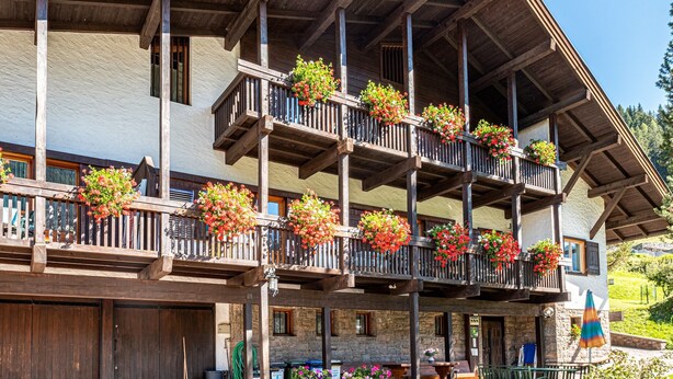 Un immeuble à plusieurs étages, doté de balcons ornés de jardinières fleuries, d’une façade en bois et d’un socle en pierre.