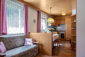 Une cuisine chaleureuse avec un îlot central en bois, une table à manger et un canapé agrémenté de coussins à motifs.