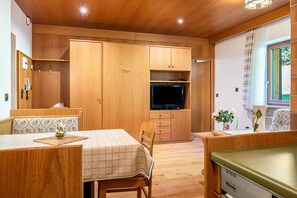 A compact kitchen with wooden cabinets, a built-in TV, and a dining area with a table and chairs.