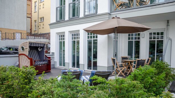 A patio with outdoor seating, including a wicker chair and foldable chairs, and a large umbrella.