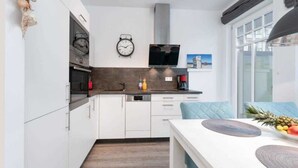 A modern kitchen with white cabinets, a dark countertop, a clock, a television, and a window with a view.