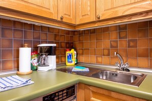 Una cocina con armarios de madera, cafetera, lavamanos y salpicadero de azulejos.
