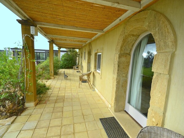 A covered patio area with a tiled floor, outdoor furniture, and a large window.