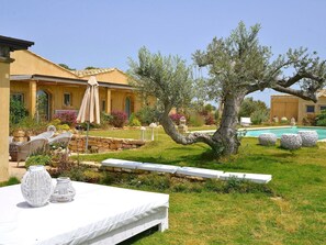 A villa with a swimming pool, outdoor seating, and a garden with olive trees.