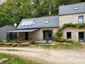 A stone house with a sloped roof, a front porch, and a satellite dish. - The 18th-century barn at the Kerguerhent Mill, along with its river, forest, and meadows.   (Pouldergat)