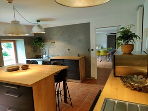 A modern kitchen with a wooden island, pendant lights, and a view into the dining area. - The 18th-century barn at the Kerguerhent Mill, along with its river, forest, and meadows.   (Pouldergat)