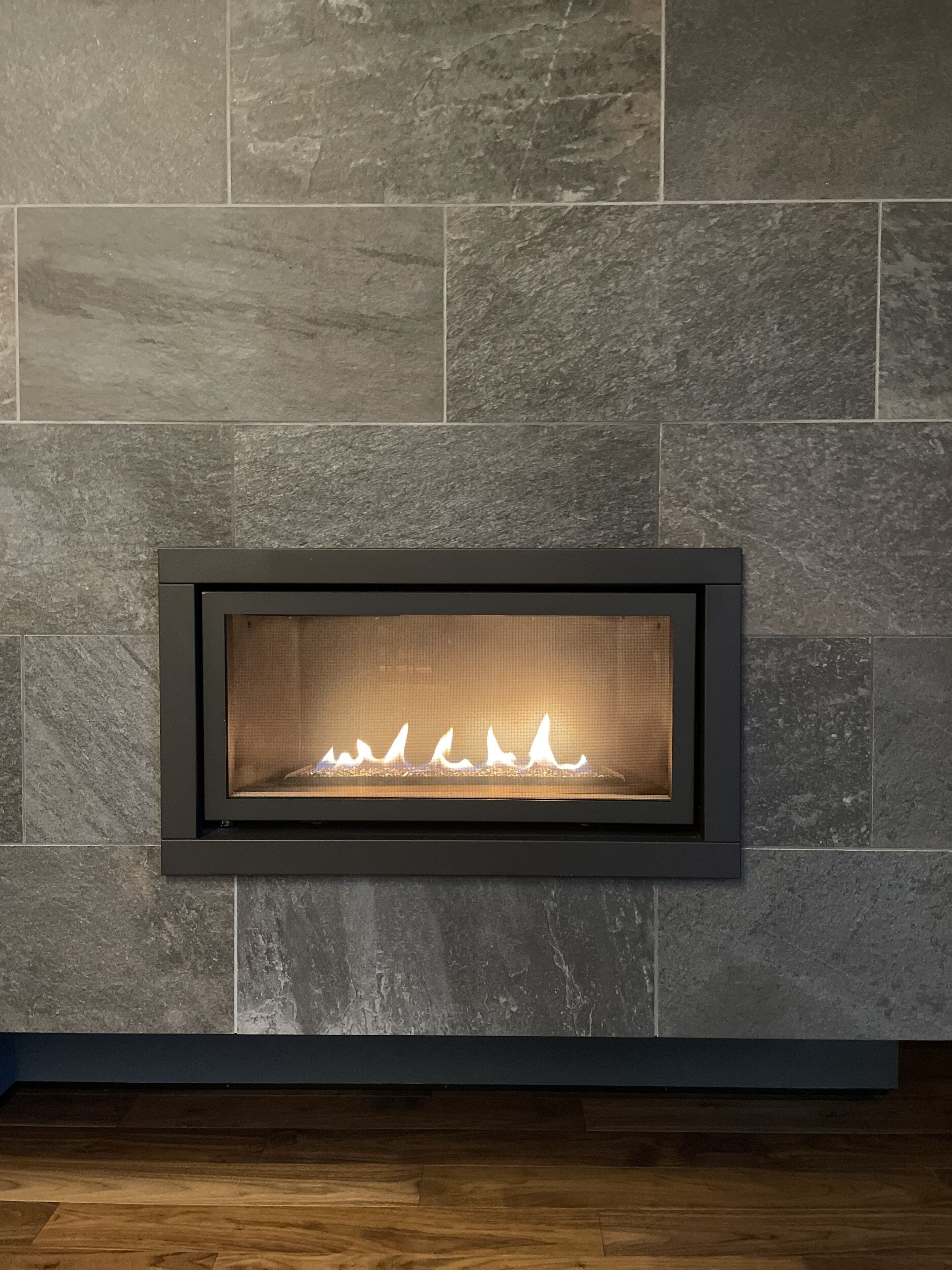 A modern fireplace with a stone wall backdrop and a dark frame.