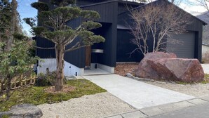 Ein modernes Gebäude mit dunkler Fassade, einem gut sichtbaren Eingang und einem gepflegten Garten mit Steinen und Bäumen.