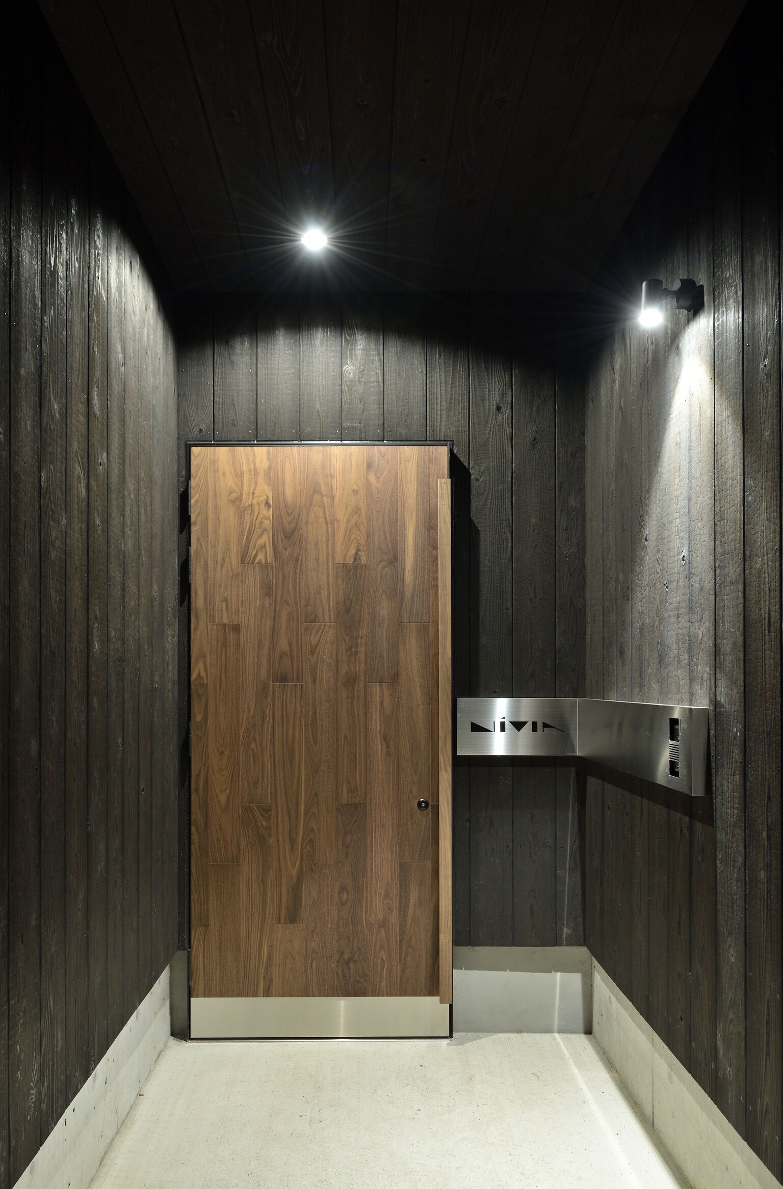 A wooden-paneled room with a wooden door, a light fixture, and a wall-mounted control panel.