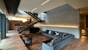 Ein modernes Wohnzimmer mit grauem Sofa, Holzboden, einer Treppe und einem Essbereich mit Tisch und Stühlen.