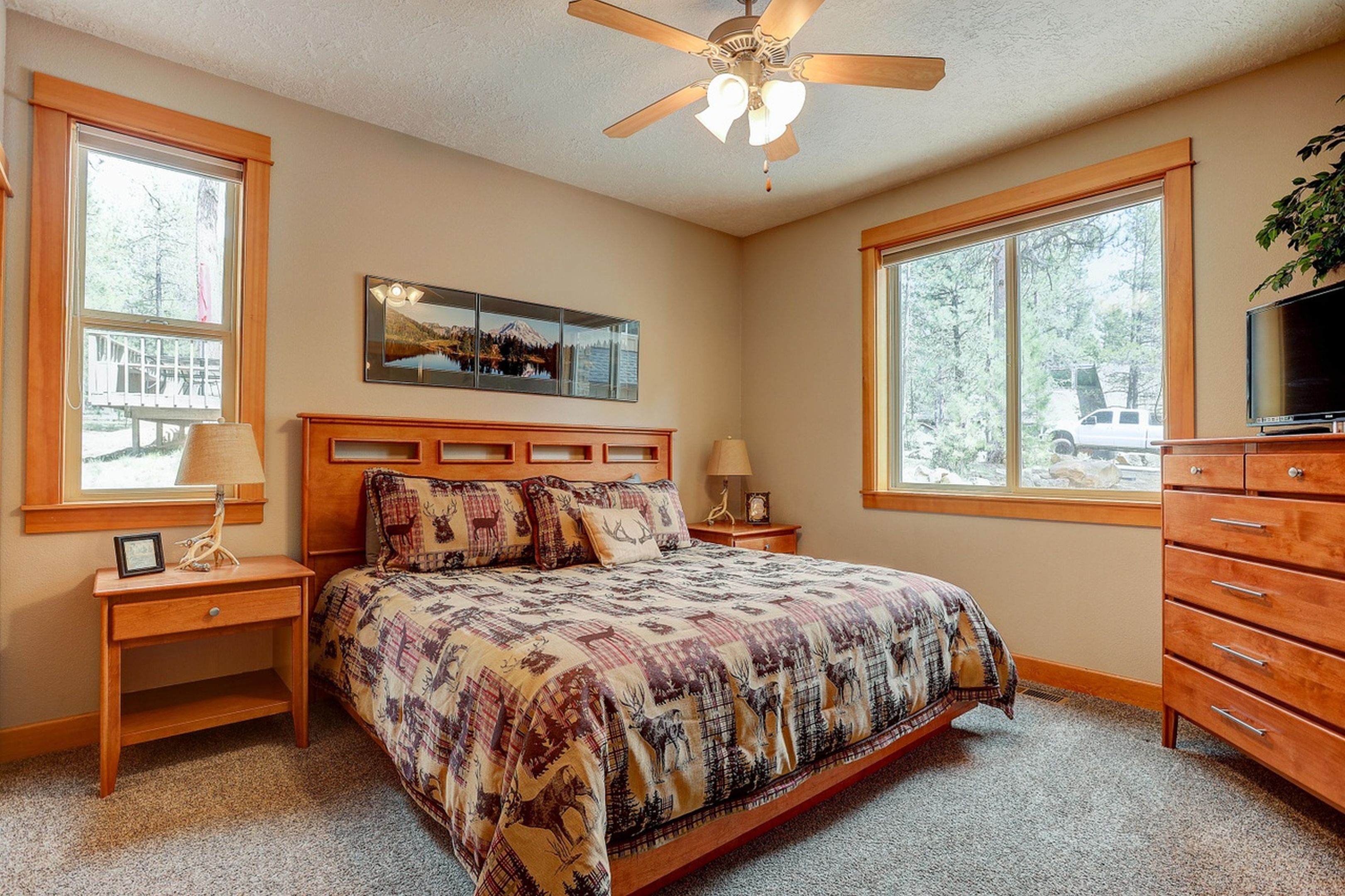 A bedroom with a bed, nightstands, a dresser, a ceiling fan, and large windows.