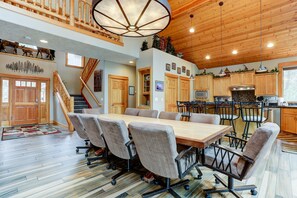 A spacious dining area with a long wooden table and multiple chairs, a kitchen with wooden cabinets and modern appliances, and a staircase leading to an upper level. - 5BR+Bunk,5.5BA,4 King,Near SHARC Pool,Hot tub,WiFi,A/C,Bikes,EV Chrg (Sunriver)