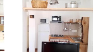 Un espacio habitable compacto con kitchenette, un televisor de pantalla plana y un estante de madera con diversos objetos.