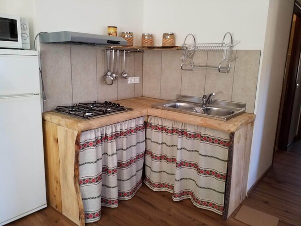 Eine kleine Küche mit Gaskochfeld, Spüle, hängenden Küchenutensilien und Gewürzgläsern.