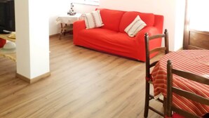 Una sala de estar con un sofá rojo, una mesa de comedor con sillas, un televisor y un cuadro en la pared.