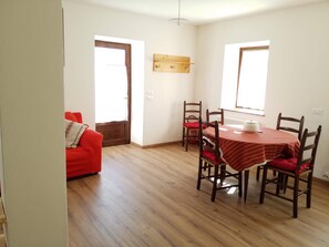 Ein Essbereich mit Holztisch und Stühlen, einem roten Sofa und einem Holzregal über dem Tisch.