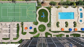 Vista aérea de un hotel con cancha de tenis, piscina y zonas de estar al aire libre.