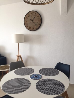 A round dining table with four black and white patterned placemats, a clock with Roman numerals, and a floor lamp. - CASA NAUTICA DEL PUERTO (LA VILA JOIOSA)
