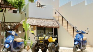 Two scooters parked in a courtyard with a thatched-roof structure and a staircase leading to an upper level. - Awesome jungle villa with pool La Veleta (Tulum)