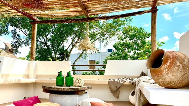 An outdoor seating area with a thatched roof, a large clay pot, and two green bottles. - Awesome jungle villa with pool La Veleta (Tulum)