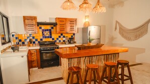 A kitchen with wooden cabinets, a stainless steel refrigerator, a wooden bar counter with stools, and a colorful tiled backsplash. - Awesome jungle villa with pool La Veleta (Tulum)